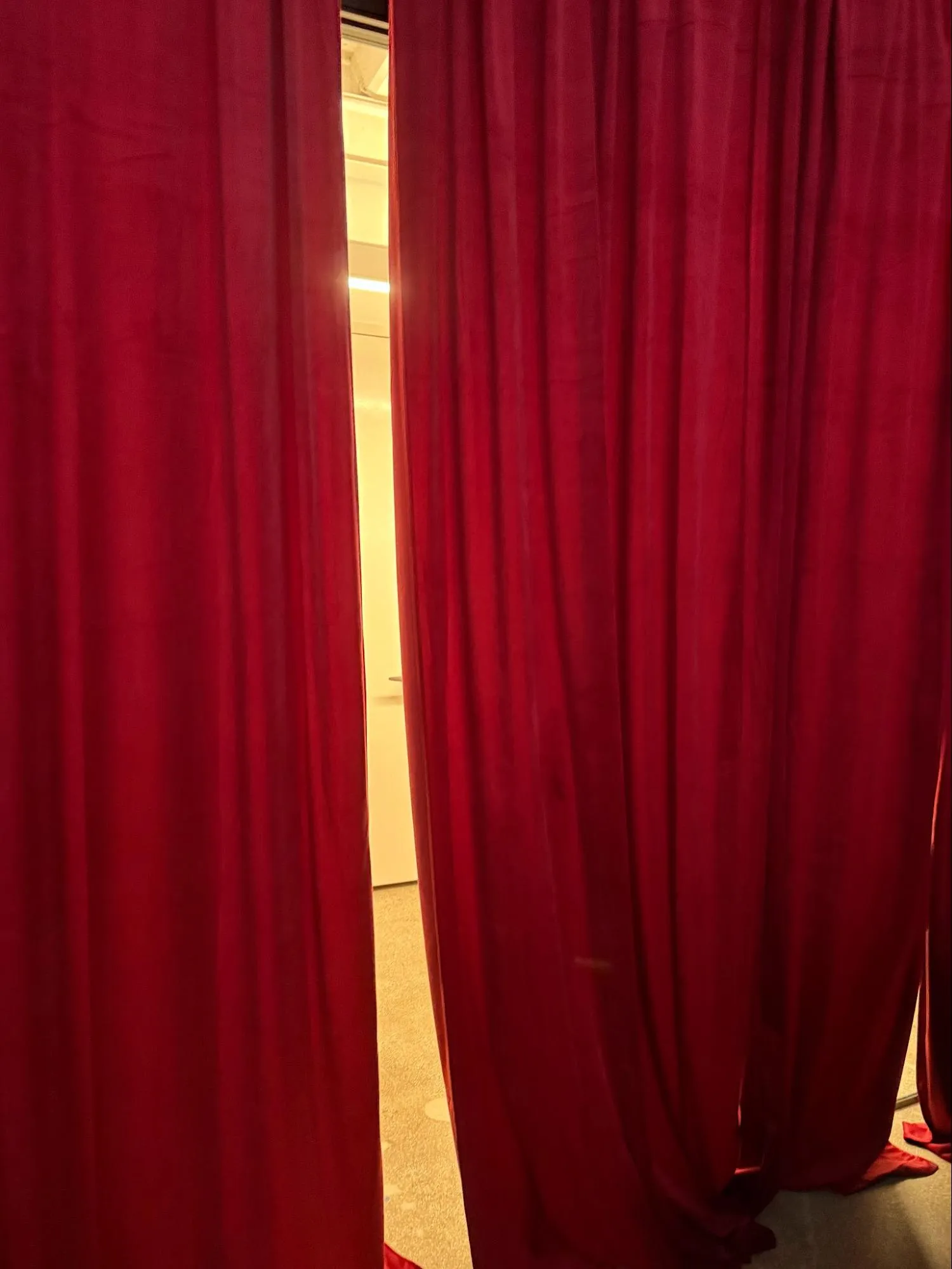 Deep red velvet curtains parted to reveal a brightly lit office hallway