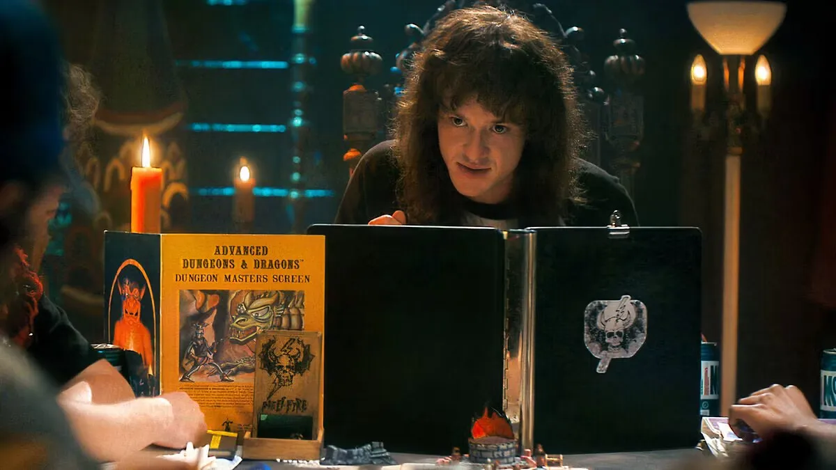 Eddie Munson leaning over a Dungeon Masters screen at a candlelit table in Stranger Things
