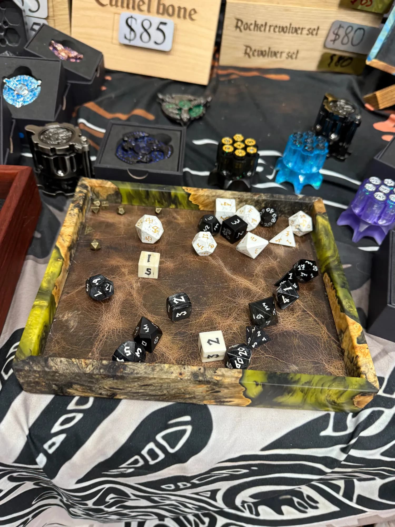 A dice tray filled with carved dice sets on a vendor table full of dice boxes and rollers